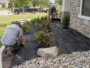 Landscape crew installing weed barrier fabric in a front yard bed edged with river rock
