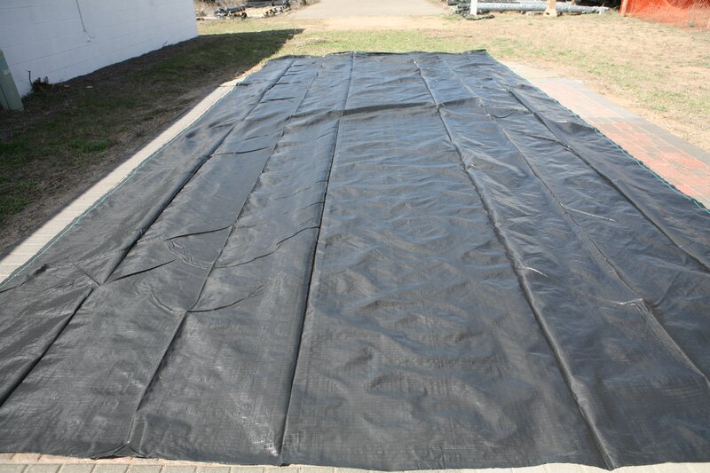 Woven ground cover fabric laid out over a paved driveway area before trimming and installation
