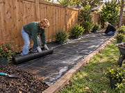 Landscape crew installing woven ground cover fabric in a commercial parking lot planting island
