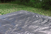 Woven ground cover fabric rolled out across a lawn edge next to a wooded area
