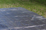 Woven ground cover fabric being unrolled further across a grassy lawn area
